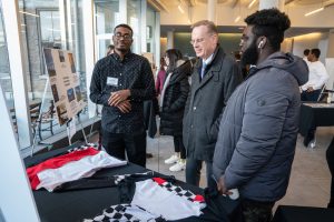 Chancellor Syverud standing in a large room between two students looking at their presentation on a table.